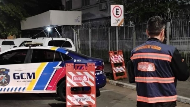 agente de trânsito da balada segura do detranrs de costas no canto direito e no canto esquerdo um veículo da guarda municipal de são leopoldo