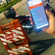 Celular com dados de veículo à direita. À esquerda um cavalete da balada segura e ao fundo uma motocicleta